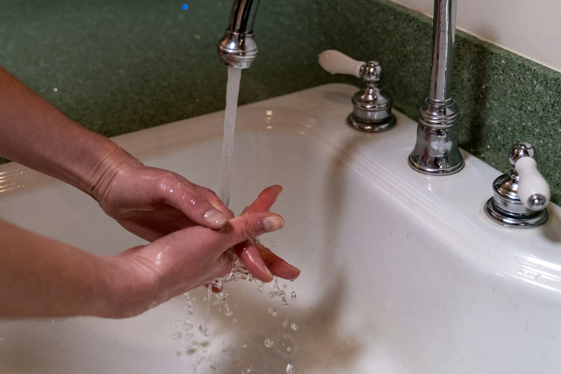 Hands being washed under running water from a chrome tap over a white basin